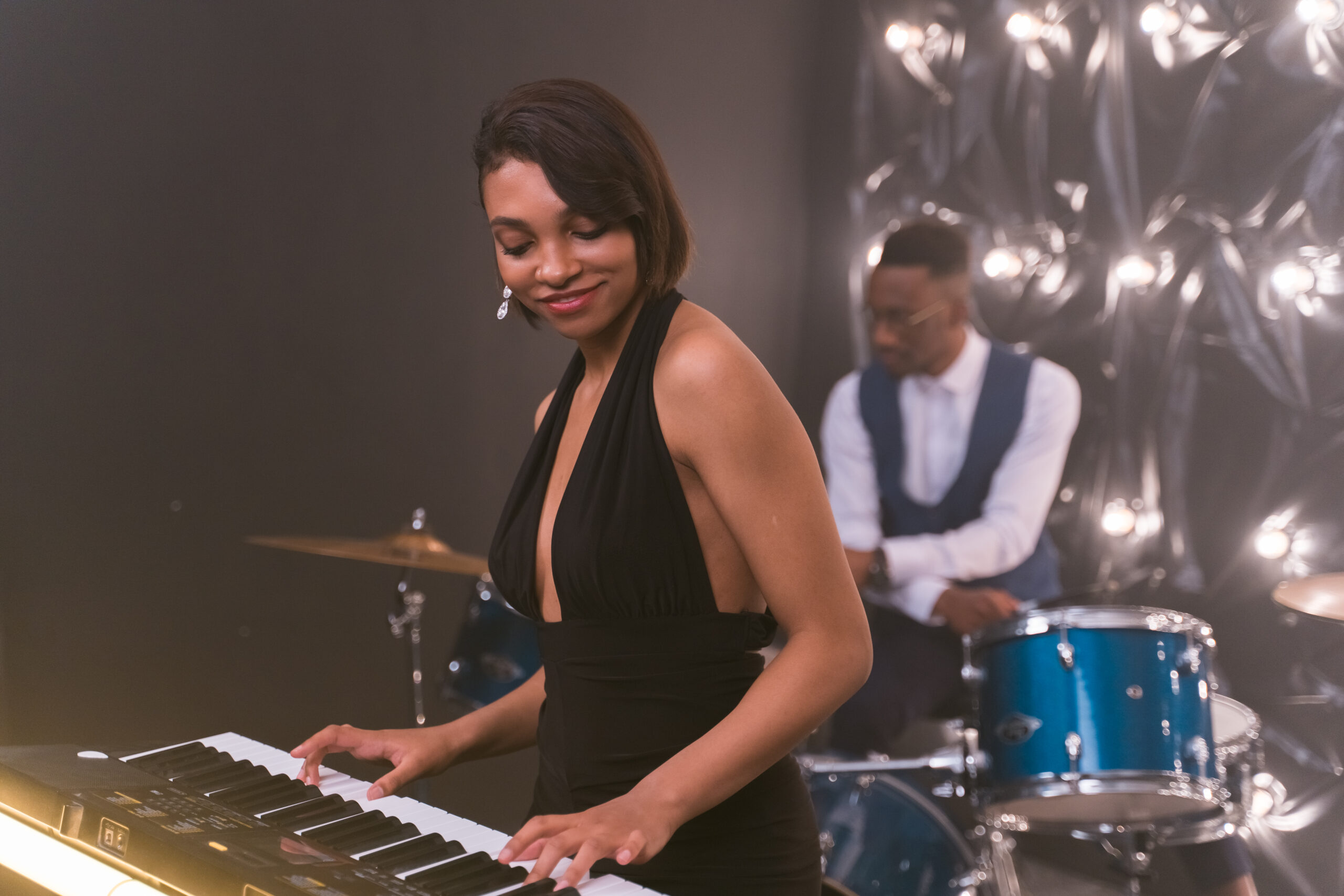 Woman playing a keyboard and a man playing the drums in the back